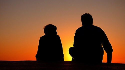Father and son facing sunset