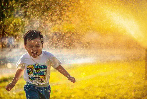 Little Boy Smiling And Running As Water Falls On Him Edited