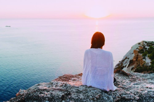 Woman Sat On Cliff Looking Towards Horizon